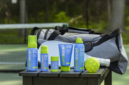 A line up of Picklebalm pain relief products on a bench next to a pickleball court