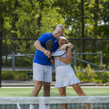 Two people hugging on a pickleball court with trees in the background